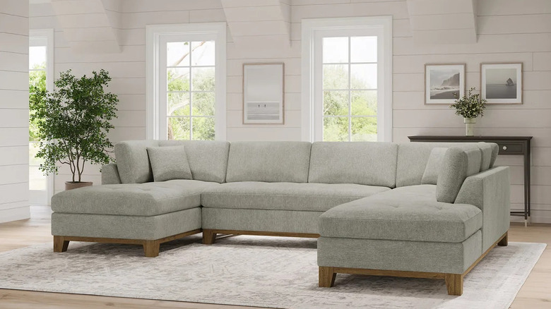 A light gray U-shaped sectional with wooden detailing in a light-filled living room