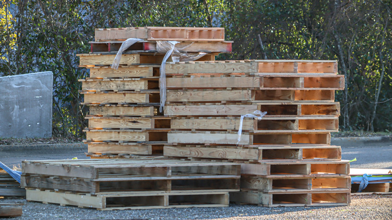 Stack of many empty, unused wood pallets on asphalt outdoors