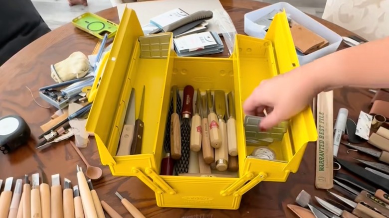 Woman placing wood carving tools in yellow toolbox