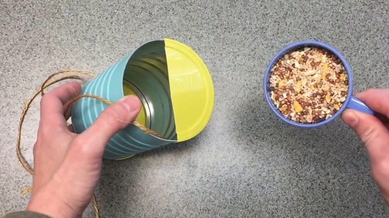 Woman filling DIY coffee container bird feeder with bird seed above countertop