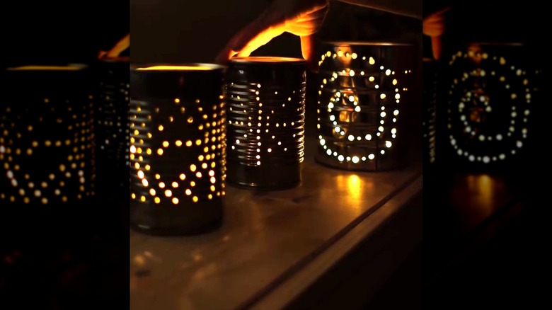 Hand turning light-up tin can lanterns made from coffee cylinders on a dark night