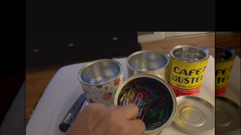 DIYer tilting repurposed coffee tin being used to house paperclips alongside other organizers