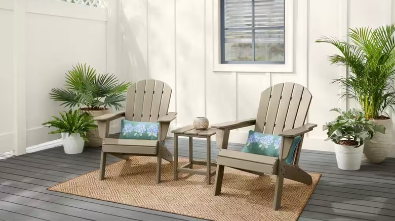 Two tan Adirondack chairs with blue pillows sit on a sisal patio rug