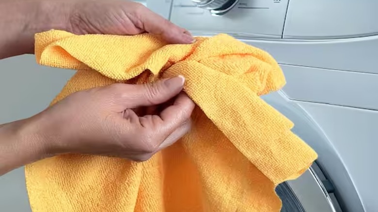 A person holds an orange microfiber cloth in front of a washing machine