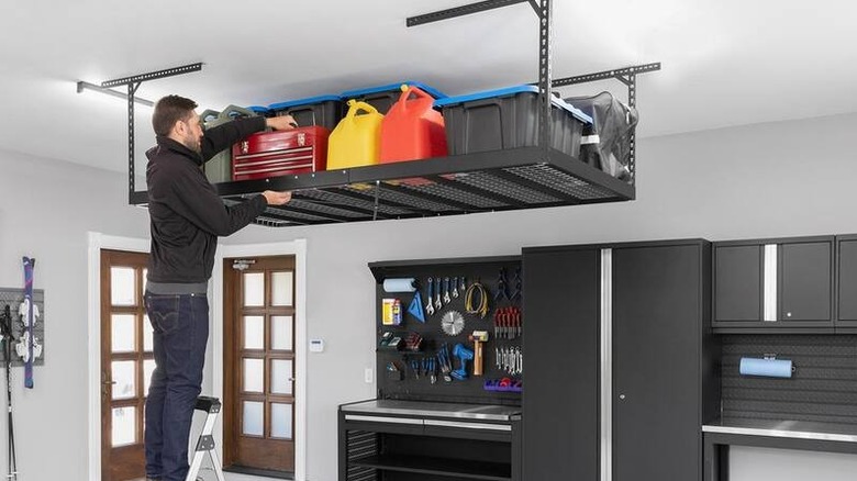 A man using a NewAge Products VersaRac Pro height-adjustable overhead rack to grab a toolbox