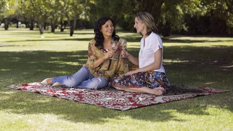 A pair of women sitting on a Nuu Garden red and white Moroccan indoor/outdoor area rug outside