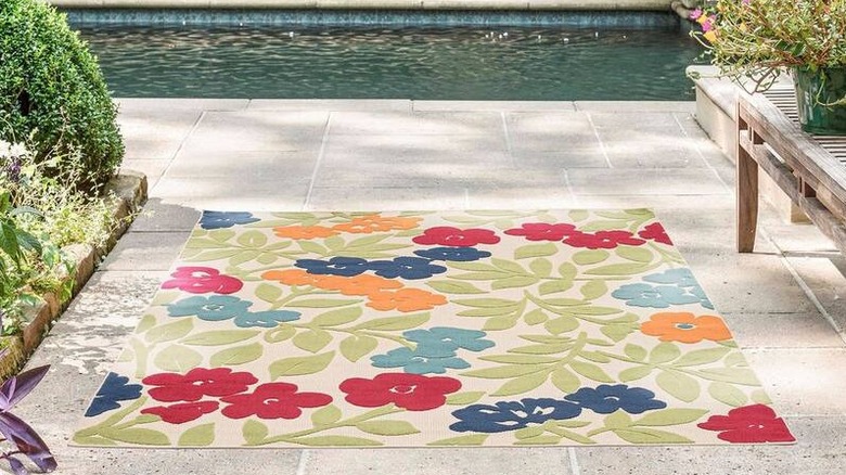 A Tayse Rugs Oasis floral indoor/outdoor area rug on a concrete tile floor outside