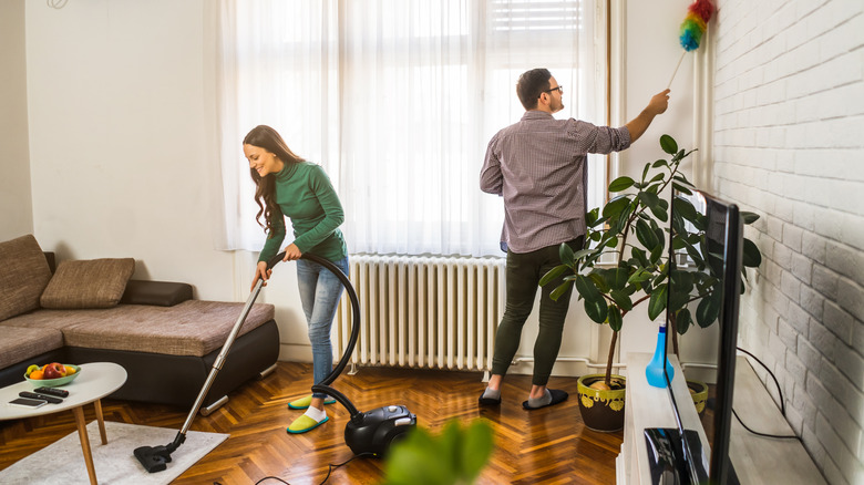 Man dusting wall while a woman vacuums floor