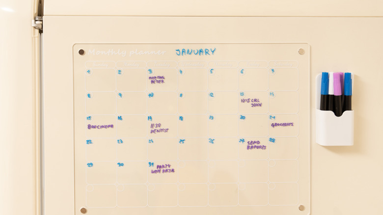 A dry erase calendar with colored markers and an eraser