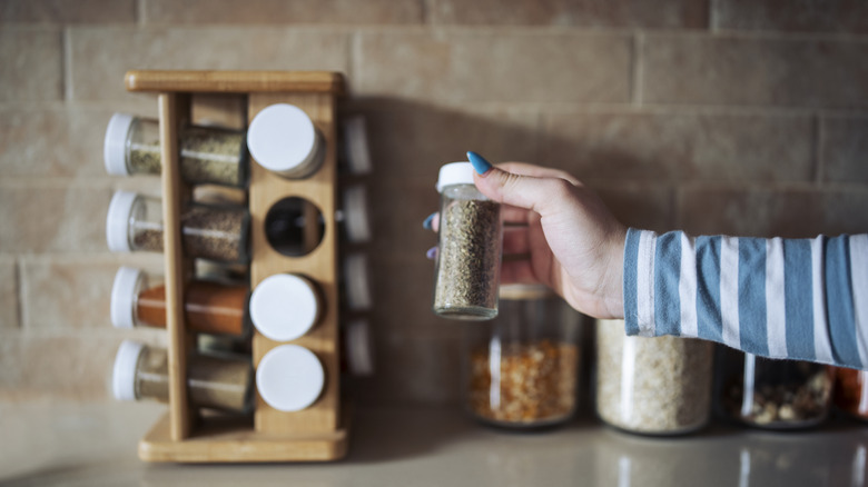 Person pulling herb out of wooden spice rack