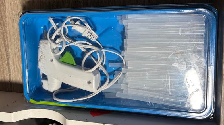 A coiled up hot glue gun and mini glue sticks tucked in plastic container in desk drawer