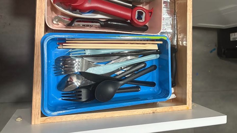 Cluttered utensils stuffed in old mop container in shallow kitchen drawer