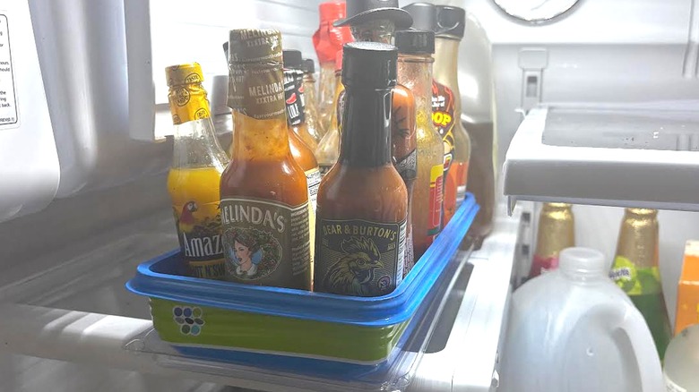 Assorted hot sauces stuffed into open Swiffer container on refrigerator shelf