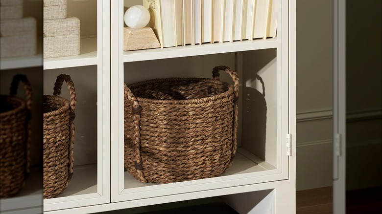 Woven round basket with handles on bottom shelf of white glass cabinet