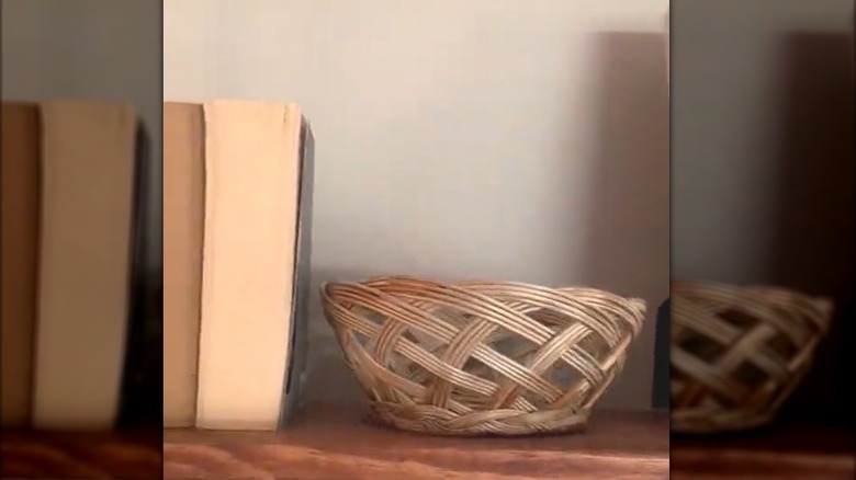 Round woven basket bowl on wood shelf beside paperback books