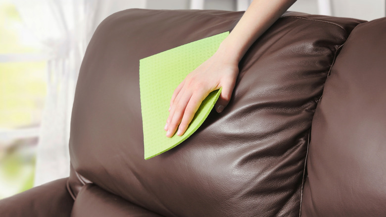 A hand using green cloth on brown leather sofa