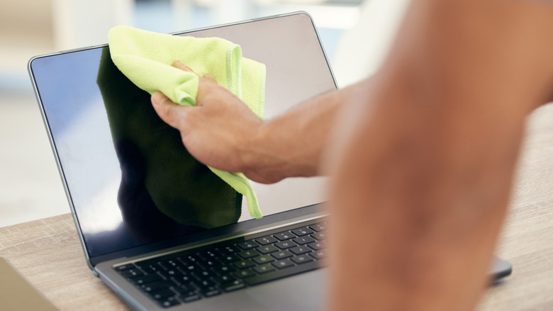 Person cleaning laptop with yellow cloth