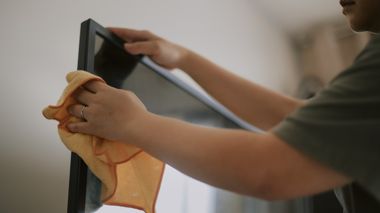Person cleaning television with an orange cloth