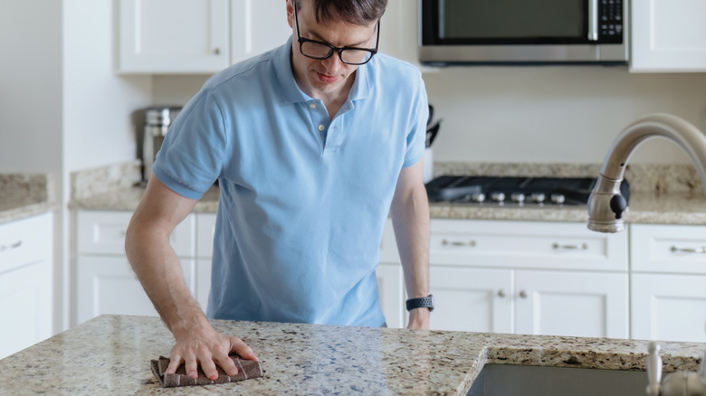 Man wiping down granite countertop in kitchen