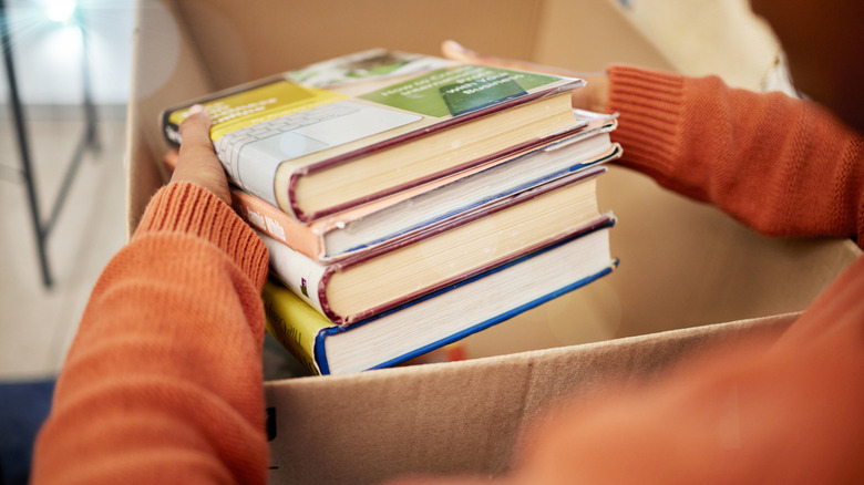 Person lifting a stack of books out of a cardboard box