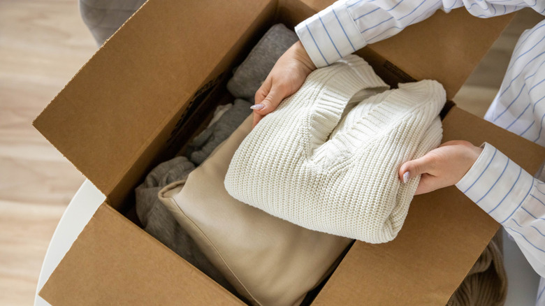 Woman packing folded sweaters into a cardboard box