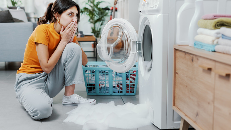 Person sitting horrified in front of their overflowing washing machine