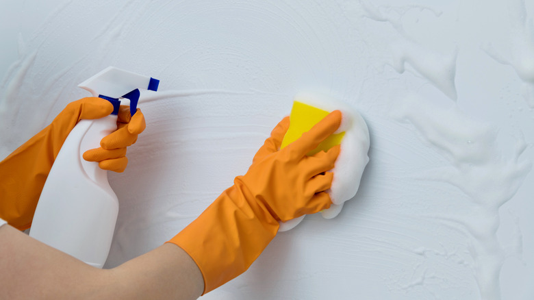 Gloved hands scrubbing a light blue wall with a soapy solution and sponge