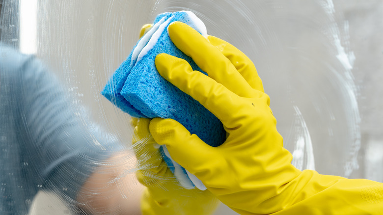 Person cleaning a mirror with a soapy sponge