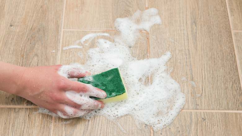 Hand scrubbing a soapy sponge on hardwood floor