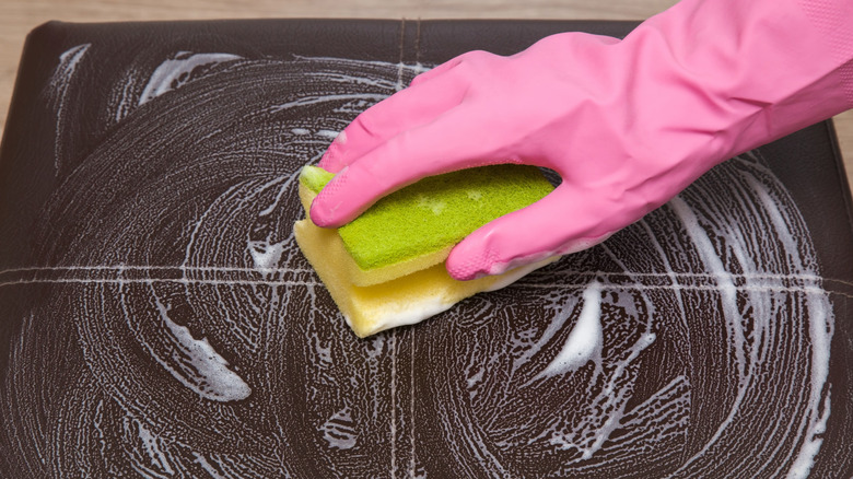 Person in pink gloved hands cleaning a leather chair with soap and a sponge
