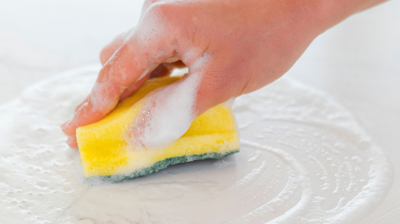Hand moving a soapy sponge over a white countertop
