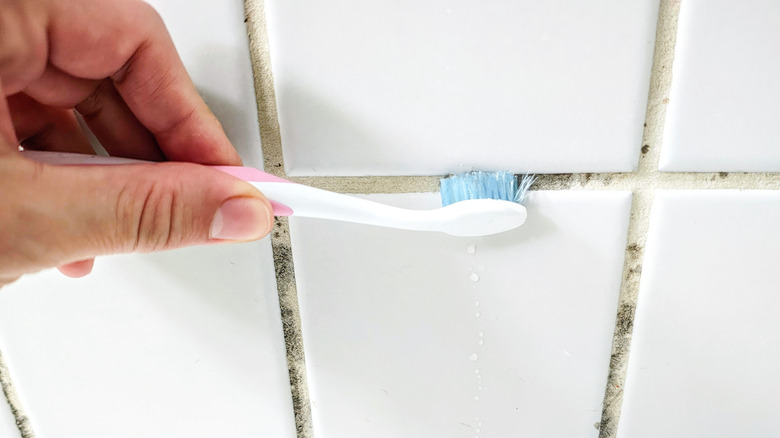 A hand uses a toothbrush to clean tile grout.