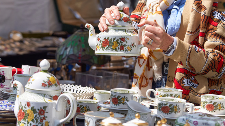 A woman holds a pretty porcelain teapot at a flea market.