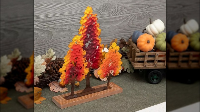 Three colorful tree decorations sit on a wooden plank