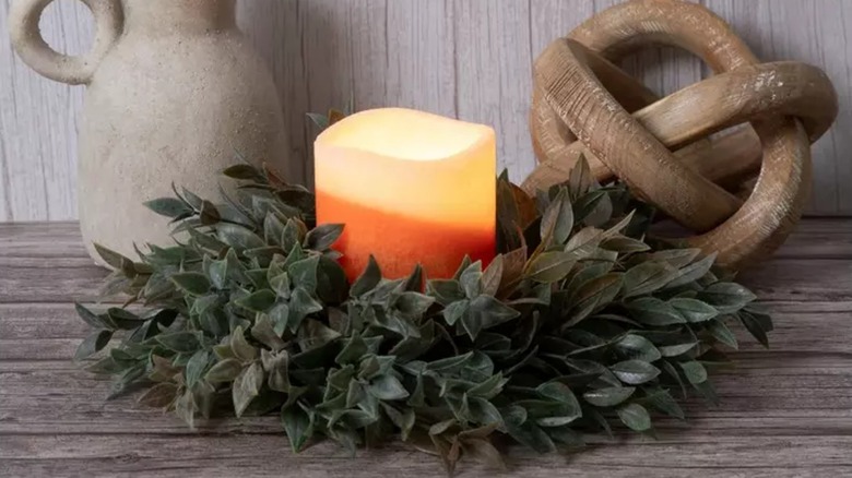 A yellow and orange candle sits inside a faux eucalyptus candle ring from Hobby Lobby