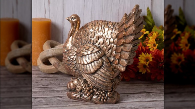 A gold metallic turkey figurine sits on a wooden table surrounded by fall decorations
