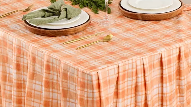 Elegant fall-colored place settings sit on a table dressed with an orange plaid ruffled flannel back tablecloth