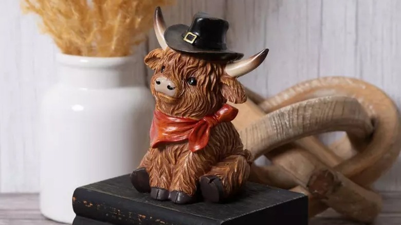 A Highland cow figurine dressed as a pilgrim sits on a stack of black books