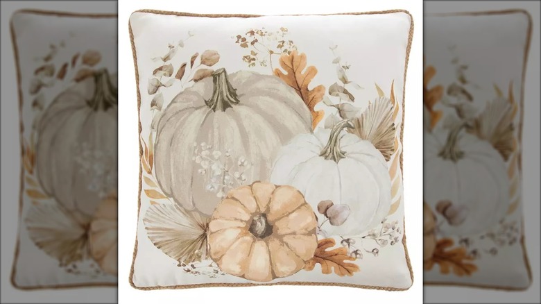 A cream throw pillow with neutral pumpkin and leaf accents is shown in a detailed shot