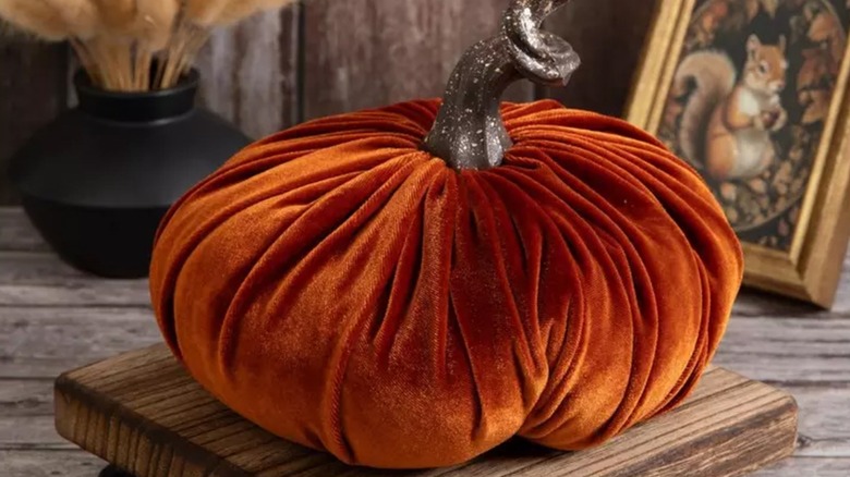 A decorative pumpkin made of orange velvet sits on a wooden table