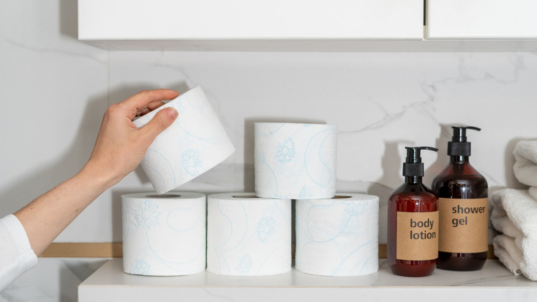 Woman stacking toilet paper rolls on bathroom shelf