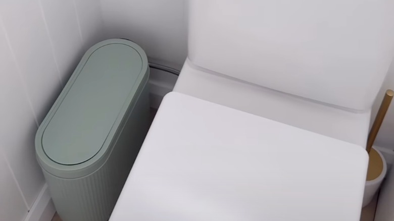 Rounded push-top trash bin next to toilet