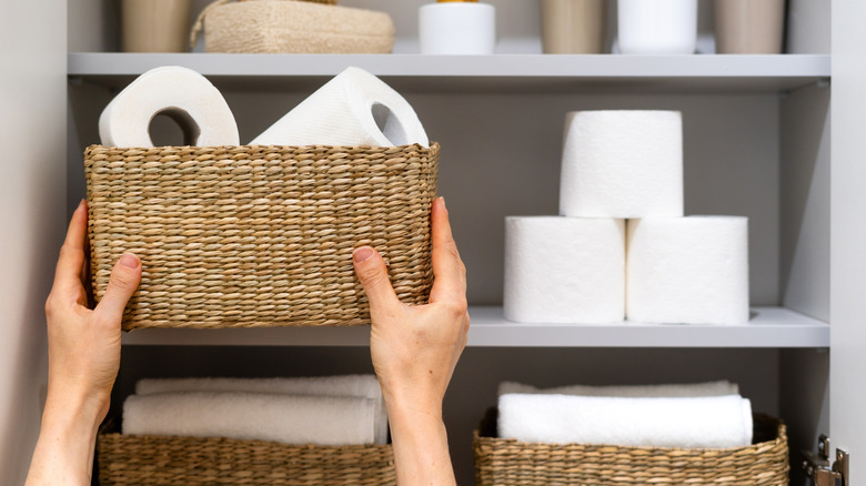 Person putting basket full of toilet paper onto bathroom shelf