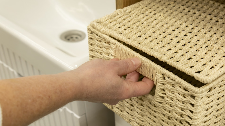 Hand pulling out lidded box from bathroom shelf