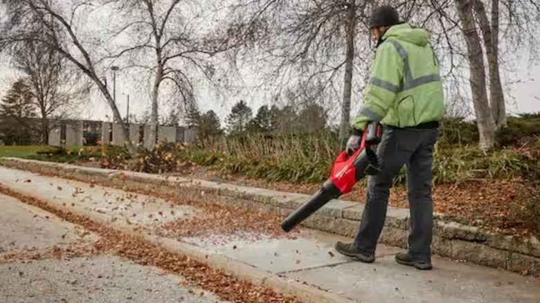 Person wearing a green jacket and using the Milwaukee blower