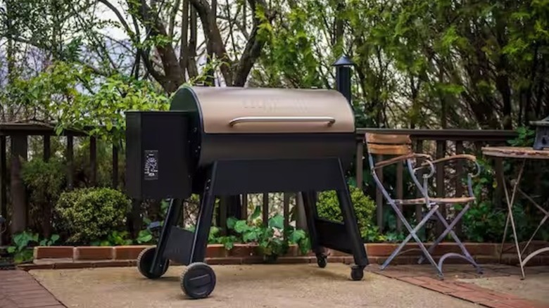 Traeger grill sitting on a deck next to a dining table with trees in the background