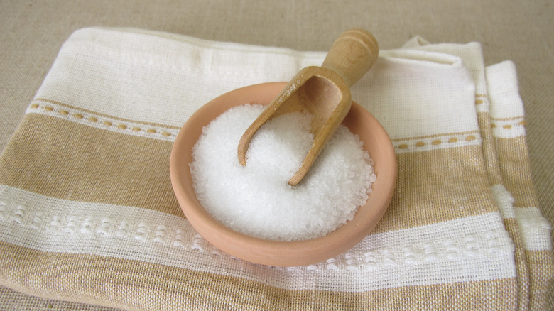 Epsom salt and wooden scoop in a terra cotta bowl atop a kitchen towel