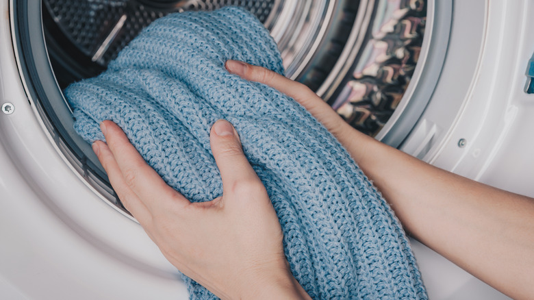 Hands removing a soft blue blanket from a laundry machine