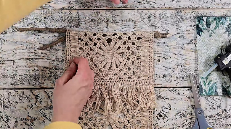 Woman wrapping rectangular beige doily around rustic stick on wood surface