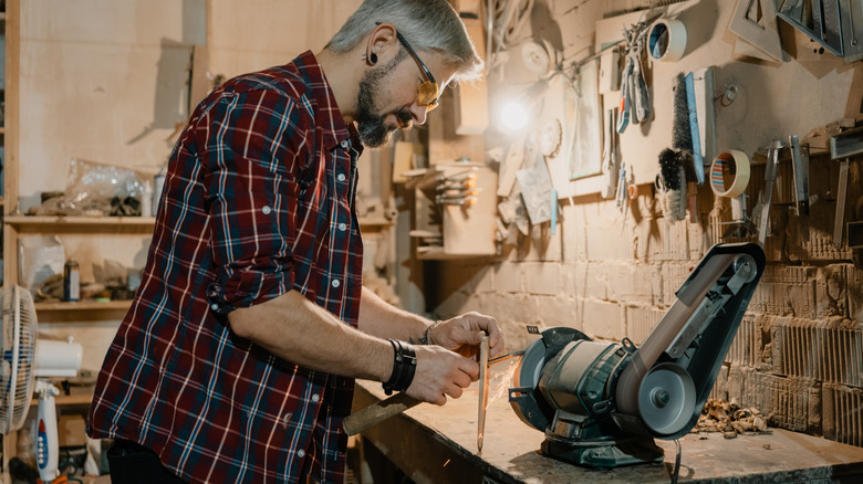 Man standing at a bench grinder sharpening a chisel